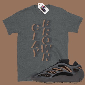 May include: A dark gray t-shirt with the word "CROWAY" in a layered, 3D design. A matching dark gray and tan sneaker is positioned below the shirt. A tag with a shoe graphic hangs from the shirt.
