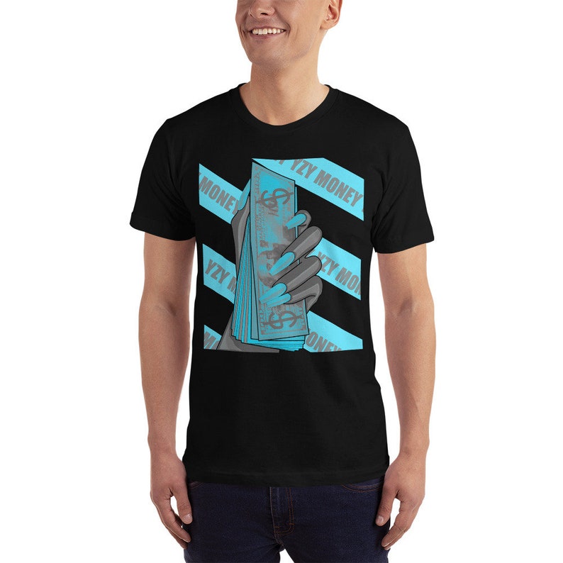 May include: Black t-shirt with a graphic of a hand holding a stack of bills. The graphic is in shades of blue and gray. The text "YZY MONEY" is repeated across the shirt in a blue and white stripe pattern.