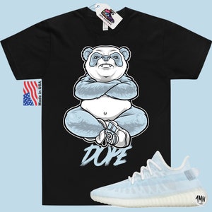 May include: Black t-shirt featuring a blue panda illustration and the word "DOPE" printed on the front. A pair of light blue and white trainers are shown below the t-shirt.