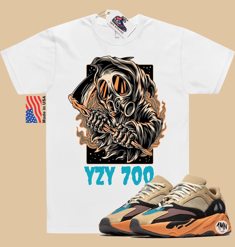 May include: White t-shirt with a graphic of a hooded figure wearing a gas mask and holding a scythe. The text "YZY 700" is printed below the graphic. A pair of tan and orange sneakers with black accents are shown below the t-shirt.