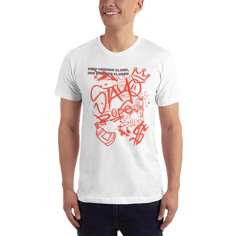 Puede incluir: Camiseta blanca con un dise&ntilde;o de graffiti rojo con las palabras "Stay DOPE" y "Keep friends close, and enemies closer".
