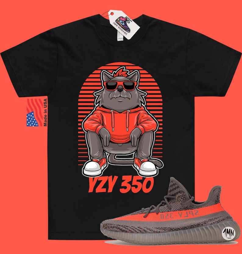 Pode incluir: Camiseta preta com um lobo de desenho animado usando &oacute;culos de sol e um moletom vermelho. O lobo est&aacute; sentado com o texto "YZY 350" abaixo. Um par de t&ecirc;nis Yeezy 350 cinza e laranja est&atilde;o no canto inferior direito da imagem.