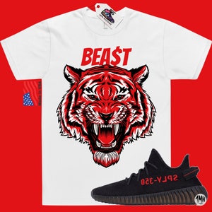 May include: White t-shirt with a red tiger graphic and the word "BEAST" in red. A black and red Yeezy 350 Boost sneaker is shown below the t-shirt.