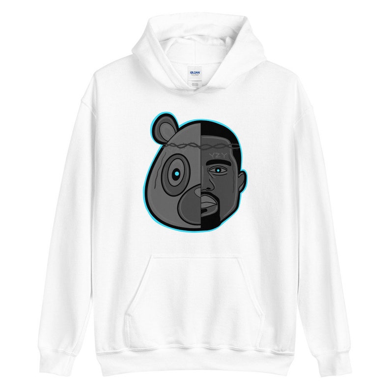 Peut inclure: Sweat-shirt &agrave; capuche blanc avec un motif noir et blanc d'une t&ecirc;te d'ours et du visage de Kanye West. Le motif est divis&eacute; en deux par une cl&ocirc;ture en fil barbel&eacute; qui s&eacute;pare les deux images. L'&oelig;il de l'ours est bleu et le texte "YZY" est visible sur le front de Kanye West.