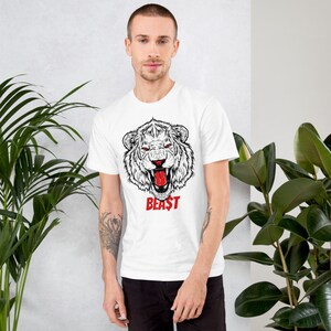 May include: White t-shirt with a black and white illustration of a roaring lion's head. The lion has a red tongue and the word "BEAST" is printed in red below the lion's head.