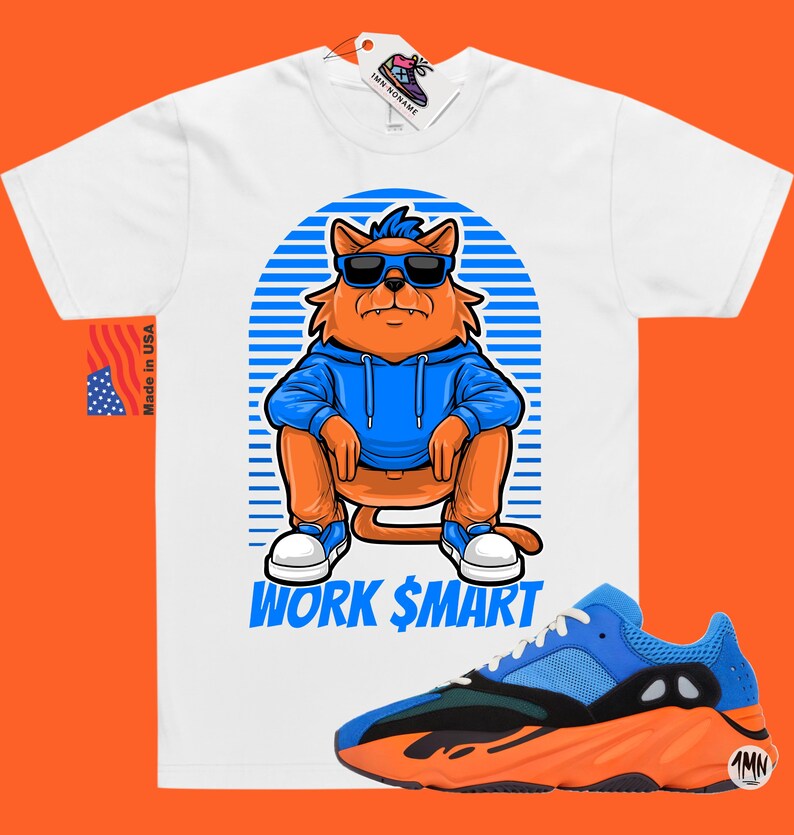 Op de afbeelding: Wit T-shirt met een cartoonkat die een zonnebril en een blauwe hoodie draagt. De kat zit met de tekst "WORK $MART" eronder. Een paar oranje en blauwe sneakers bevinden zich in de rechterbenedenhoek van de afbeelding.