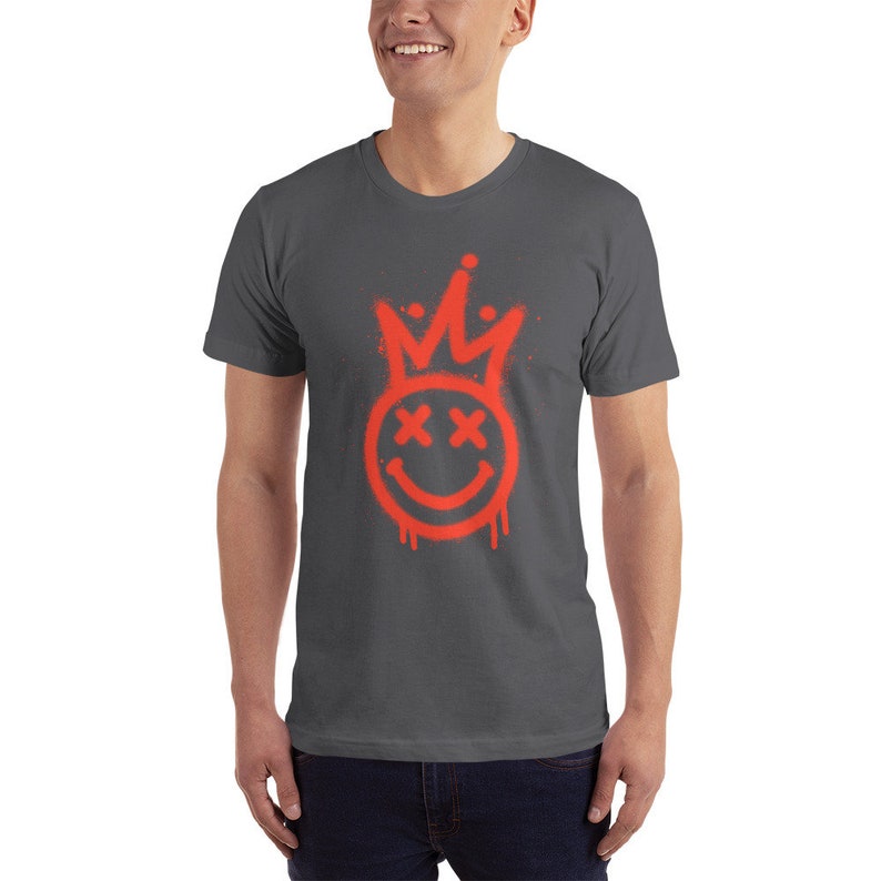 May include: A dark grey t-shirt featuring a red spray paint design of a smiley face with a crown on top. The smiley face has X's for eyes.