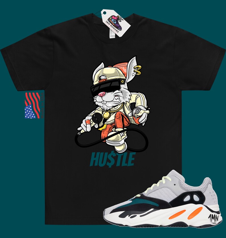 May include: Black t-shirt featuring a cartoon rabbit wearing sunglasses and a hat, holding a microphone and spray paint can. The text "HUSTLE" is printed below the rabbit. A pair of white, grey, orange, and teal trainers are shown below the t-shirt.