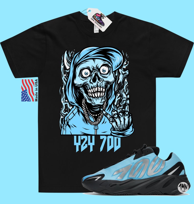 May include: Black t-shirt with a blue and white illustration of a skull wearing a hoodie and a chain. The text "424 700" is printed below the illustration. A pair of blue and black sneakers with the text "700" on the side are also shown.