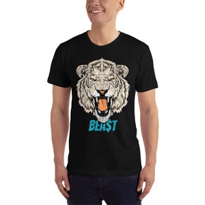 May include: Black t-shirt featuring a detailed illustration of a white tiger's head with orange eyes and an open mouth. The word "BEA$T" is printed in blue below the tiger's head. The shirt is short-sleeved.
