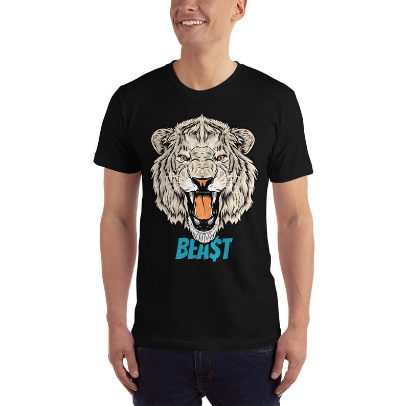 May include: Black t-shirt featuring a detailed illustration of a white tiger's head with orange eyes and an open mouth. The word "BEA$T" is printed in blue below the tiger's head. The shirt is short-sleeved.