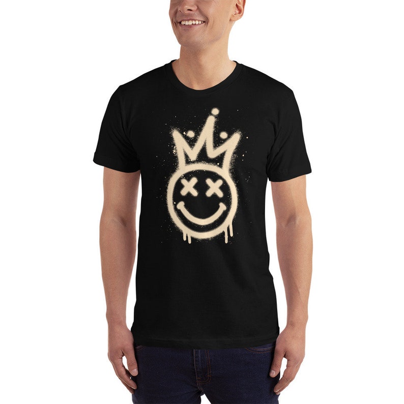 Puede incluir: Camiseta negra con un dise&ntilde;o de pintura en aerosol blanco de una cara sonriente con una corona en la parte superior. La cara sonriente tiene X para los ojos.