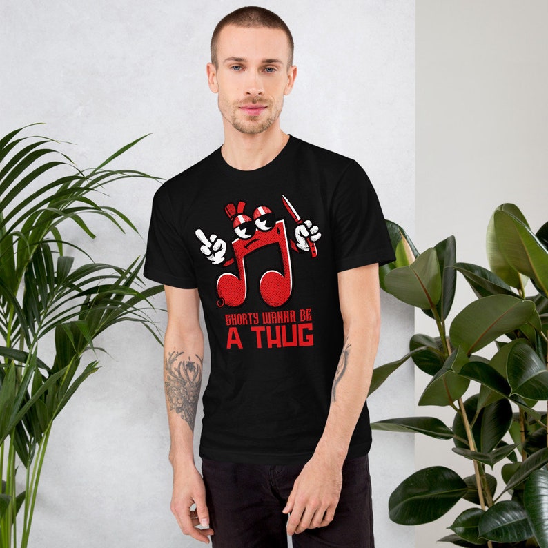 Puede incluir: Camiseta negra con un gr&aacute;fico de nota musical roja. La nota tiene una cara con gafas de sol y sostiene un cuchillo. El texto "Shorty Wanna Be A Thug" est&aacute; debajo de la nota.
