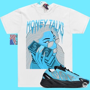 May include: White t-shirt with a blue and gray illustration of a woman with sunglasses holding a stack of money. The text "MONEY TALKS" is above the illustration. A pair of black and blue sneakers with a silver logo are in the bottom right corner of the image.