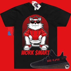 Puede incluir: Camiseta negra con un gato de dibujos animados blanco que lleva una sudadera roja y gafas de sol. El gato est&aacute; sentado con el texto "WORK $MART" debajo. Un par de zapatillas Yeezy negras y rojas se encuentran en la esquina inferior derecha de la imagen.