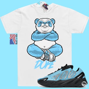 May include: White t-shirt featuring a blue panda illustration and the word "Dope" printed below. A pair of blue and black Adidas Yeezy 700 trainers are also shown.