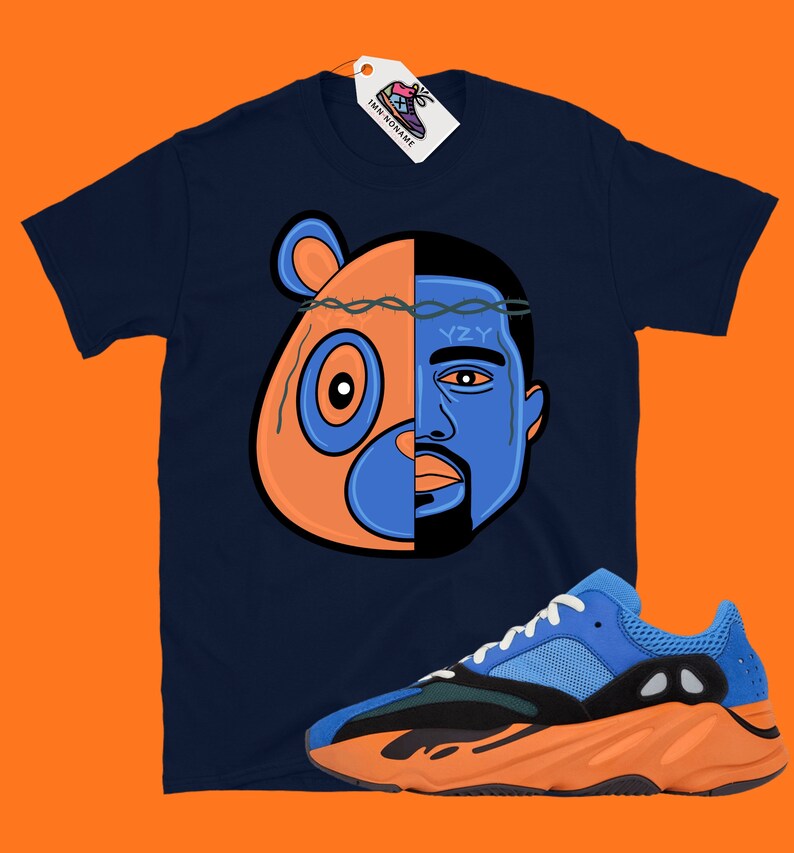 Pode incluir: Uma camiseta azul marinho com um gr&aacute;fico de um urso e o rosto de Kanye West. O gr&aacute;fico &eacute; dividido ao meio, com o urso &agrave; esquerda e Kanye &agrave; direita. O urso &eacute; laranja e azul, e Kanye &eacute; azul. A camiseta &eacute; combinada com t&ecirc;nis laranja e azul.