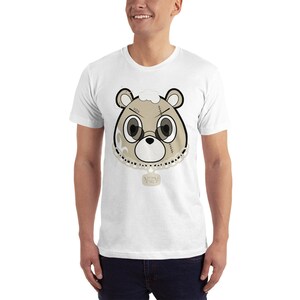 May include: White t-shirt with a cartoon bear wearing a gold chain and a tag that says "Wavy" on it. The bear has a stitched-up face and is wearing a gold chain.