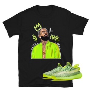 Puede incluir: Camiseta negra con una ilustraci&oacute;n verde de un hombre que lleva una chaqueta verde y una corona. El texto '#HUSTLE' est&aacute; escrito en verde. Un par de zapatillas de deporte de color verde ne&oacute;n se muestran debajo de la ilustraci&oacute;n.