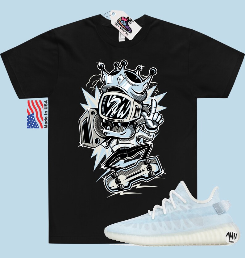 Puede incluir: Camiseta negra con una ilustraci&oacute;n de dibujos animados de un personaje que lleva una corona y sostiene una radio. El personaje est&aacute; de pie sobre una patineta. La camiseta se combina con un par de zapatillas de deporte azul claro con suela blanca.