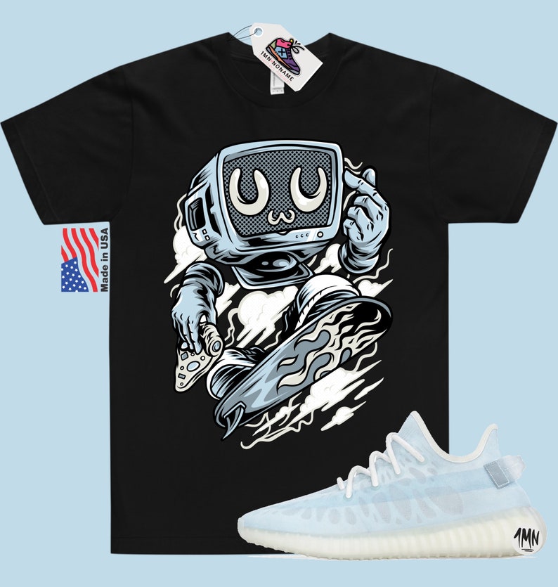 May include: Black t-shirt with a cartoon illustration of a robot with a television for a head skateboarding. The robot is wearing a blue jumpsuit and has a white cloud behind it. The t-shirt has the text "Made in USA" on the left side. A pair of white and light blue sneakers with the text "1MN" on the side are shown below the t-shirt.