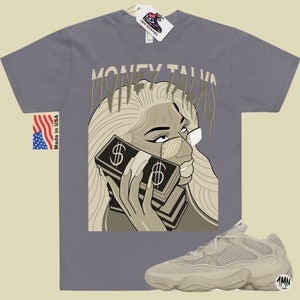 May include: A gray t-shirt with a graphic of a woman holding a stack of money with the text "Money Talks" printed on the shirt. A pair of beige sneakers with a mesh design are also pictured.