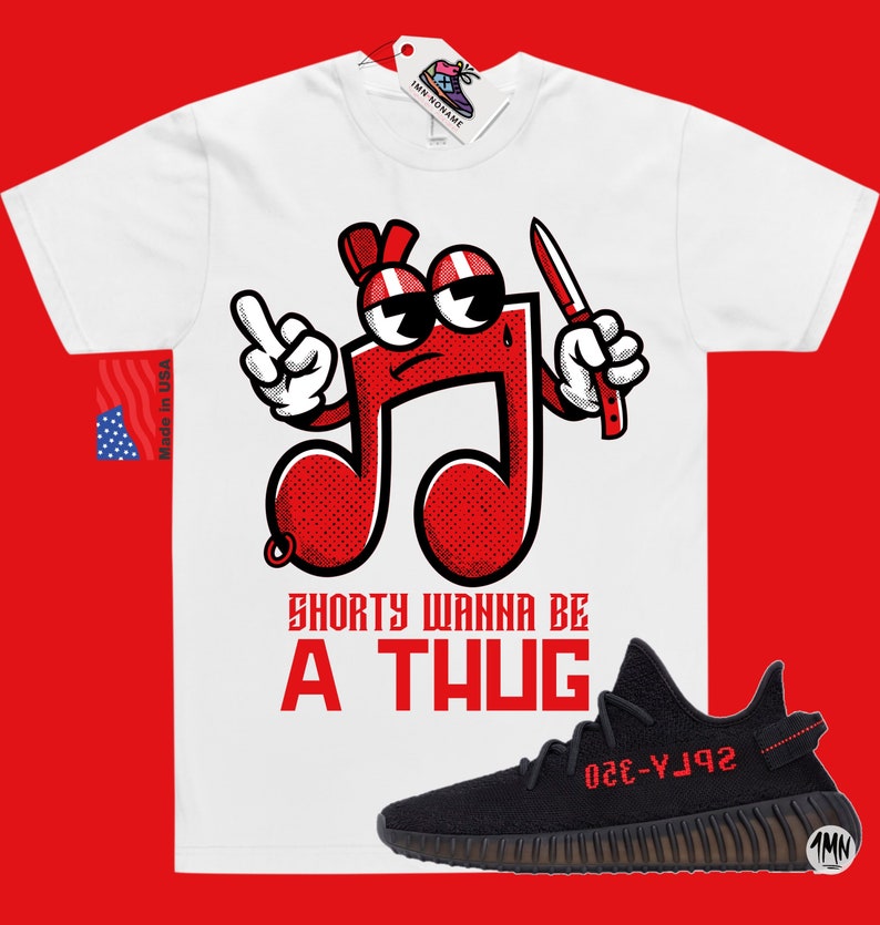 Puede incluir: Camiseta blanca con una nota musical roja de dibujos animados que sostiene un cuchillo y el texto "Shorty Wanna Be A Thug". Zapatillas negras y rojas con el texto "YZY-350" en el lateral.