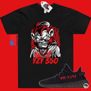 May include: Black t-shirt with a red and white illustration of a monkey wearing a hat and a chain. The text "YZY 350" is printed below the monkey. A black and red Yeezy 350 shoe is shown below the t-shirt.