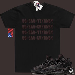 Puede incluir: Camiseta negra con el texto "00-350-YZYBABY" y "00-350-CRYBABY" repetido dos veces. Un par de zapatillas negras y grises con estampado de camuflaje.