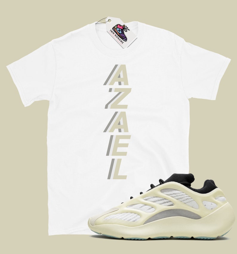May include: White t-shirt with the word "AZAEL" printed vertically in a light beige color. A pair of white and beige sneakers with black accents.