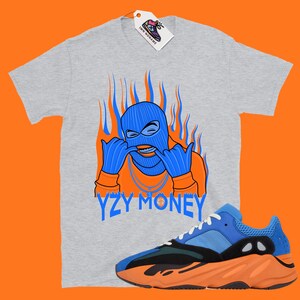 May include: A gray t-shirt with a blue and orange illustration of a person wearing a ski mask and the text "YZY MONEY". A pair of blue and orange sneakers are also pictured.
