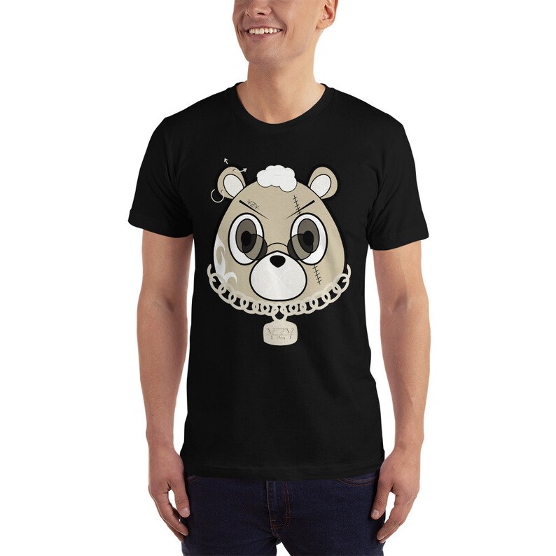 May include: Black t-shirt with a cartoon image of a brown bear wearing a gold chain and a tag that says "AZN" on it. The bear has stitches on its face and a gold hoop earring.