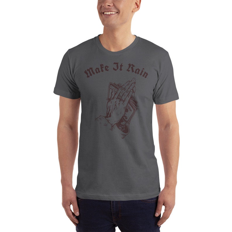 K&ouml;nnte beinhalten: Ein dunkelgraues T-Shirt mit einer Grafik einer Hand, die Geld in einer betenden Position h&auml;lt. Der Text "Make It Rain" ist in dunkelroter Schrift &uuml;ber der Grafik gedruckt.
