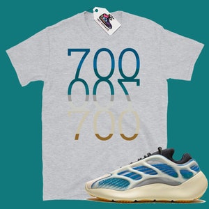 May include: A grey t-shirt with the number 700 printed in a gradient of blue, grey, and brown. A pair of white and blue trainers with a black sole.