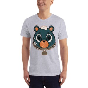 May include: A grey t-shirt featuring a cartoon bear wearing a chain with a tag that reads "YZY". The bear has a dollar sign on its head and an X over its mouth.