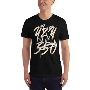 May include: Black t-shirt with a white and beige spray paint design of a crown and the text "Yeezy 350".