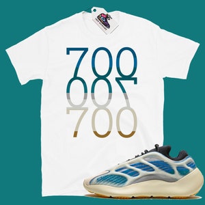 May include: White t-shirt with the numbers 700, 007, and 700 printed in a gradient of blue, grey, and brown. A pair of white and blue trainers with a black sole.