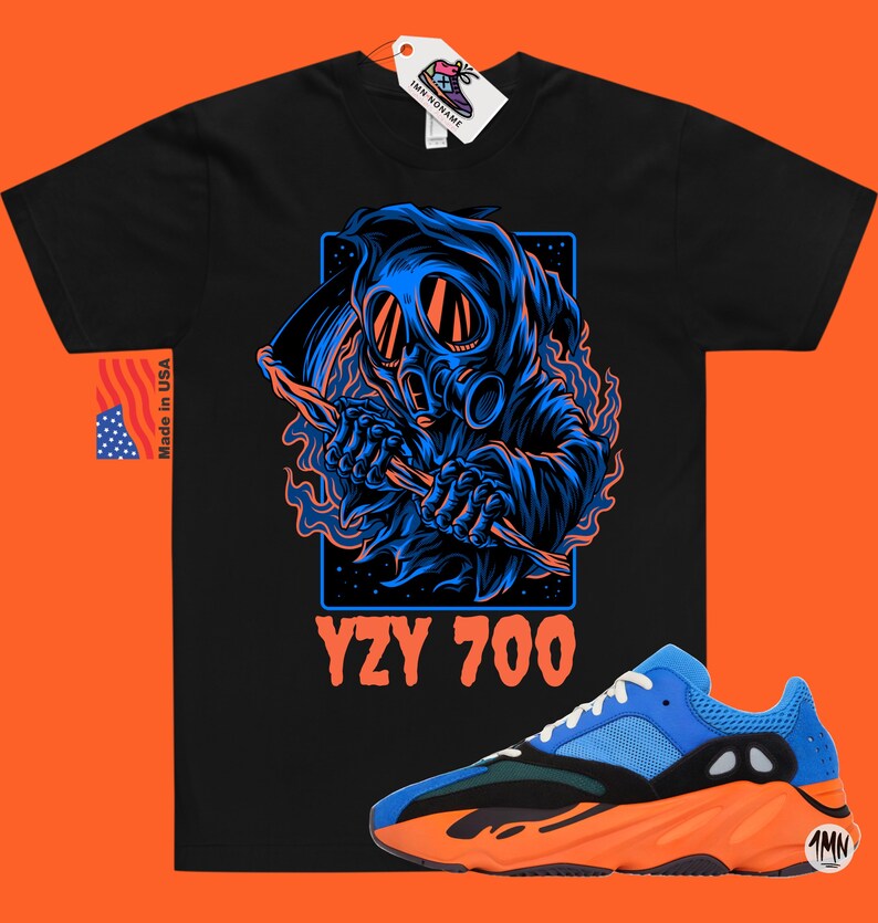 May include: Black t-shirt with a blue and black graphic of a hooded figure wearing a gas mask and holding a scythe. The text "YZY 700" is printed below the graphic. A pair of blue and orange sneakers are shown below the t-shirt.