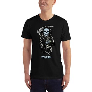 May include: A black t-shirt featuring a graphic of a blue skeletal figure in a black robe holding a flower. The figure is holding a scythe in its other hand. The text "VZY DEATH" is printed below the figure.
