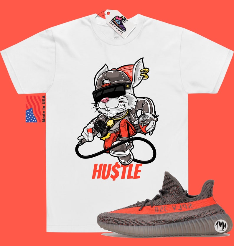 May include: White t-shirt with a cartoon rabbit wearing sunglasses, a gold chain, and a red hat. The rabbit is holding a microphone and a spray can. The text "HUSTLE" is printed below the rabbit. A pair of grey and orange sneakers are shown below the t-shirt.