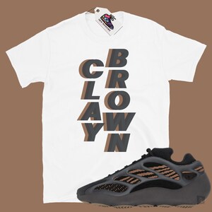 May include: White t-shirt with the word "CBRAYWN" in layered gray and brown letters. A black and brown athletic shoe is next to the shirt. A tag with a shoe logo hangs from the shirt.