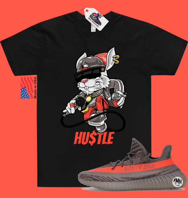 May include: Black t-shirt with a cartoon rabbit wearing sunglasses and a hat, holding a microphone. The text "HUSTLE" is printed below the rabbit. A pair of grey and orange sneakers are shown below the t-shirt.