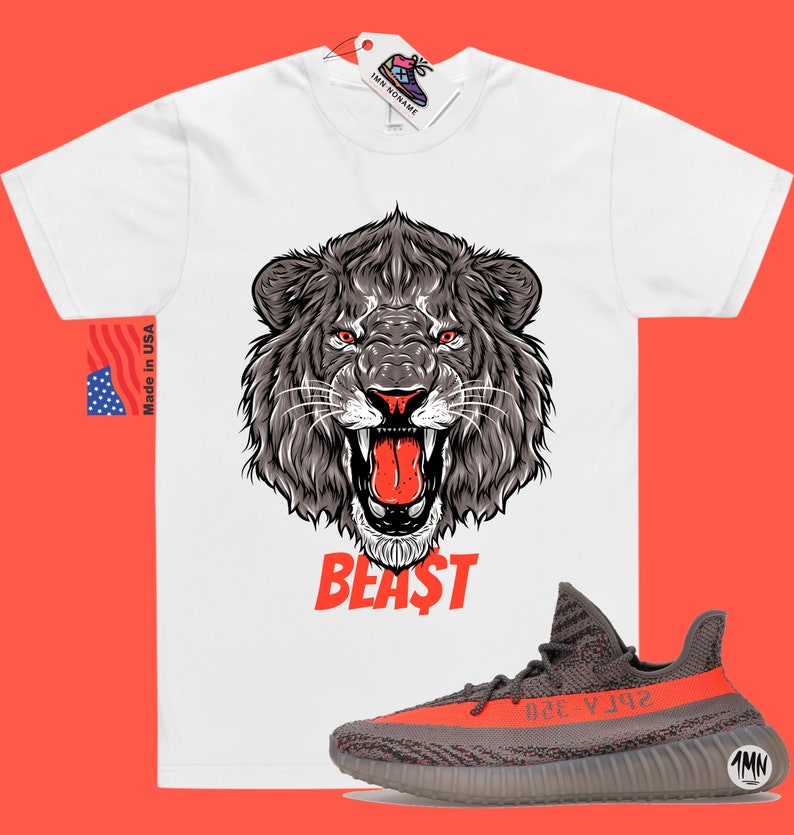 Puede incluir: Camiseta blanca con un gr&aacute;fico de la cabeza de un le&oacute;n rugiente y la palabra "BEAST" en rojo. La camiseta se combina con zapatillas grises y naranjas con el texto "YZY" en el lateral.
