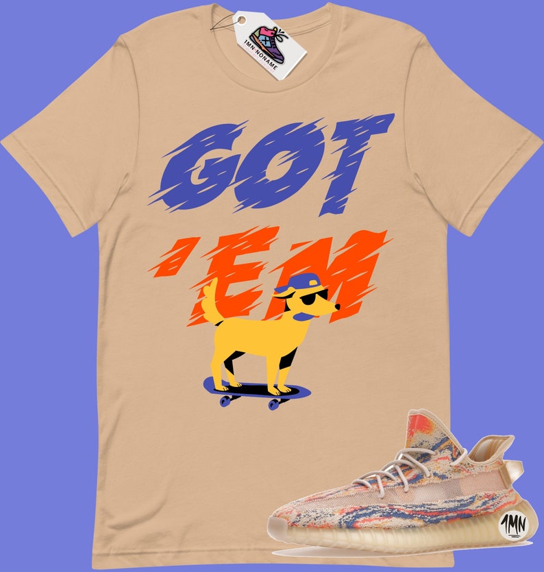 May include: A tan t-shirt with the text "GOT 'EM" in blue and orange. A cartoon dog wearing sunglasses and a blue hat is skateboarding. A pair of beige and multi-coloured trainers are shown below the t-shirt.
