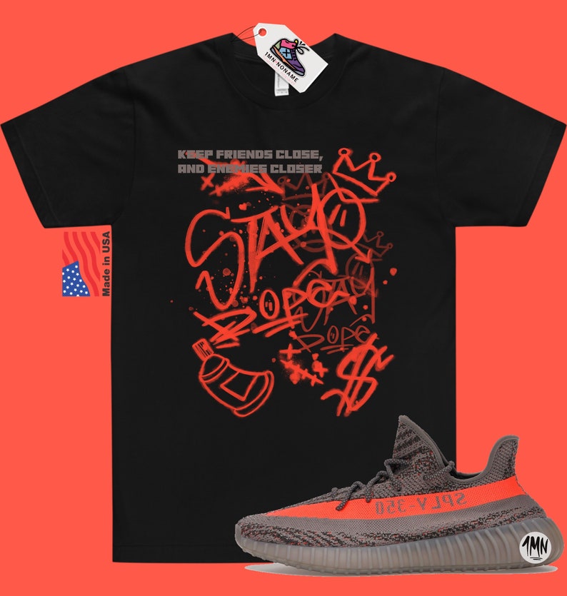 Puede incluir: Camiseta negra con estampado rojo de estilo graffiti que dice "Keep friends close, and enemies closer" y "Stay dope". Un par de zapatillas grises y naranjas con el texto "Yeezy" en el lateral.