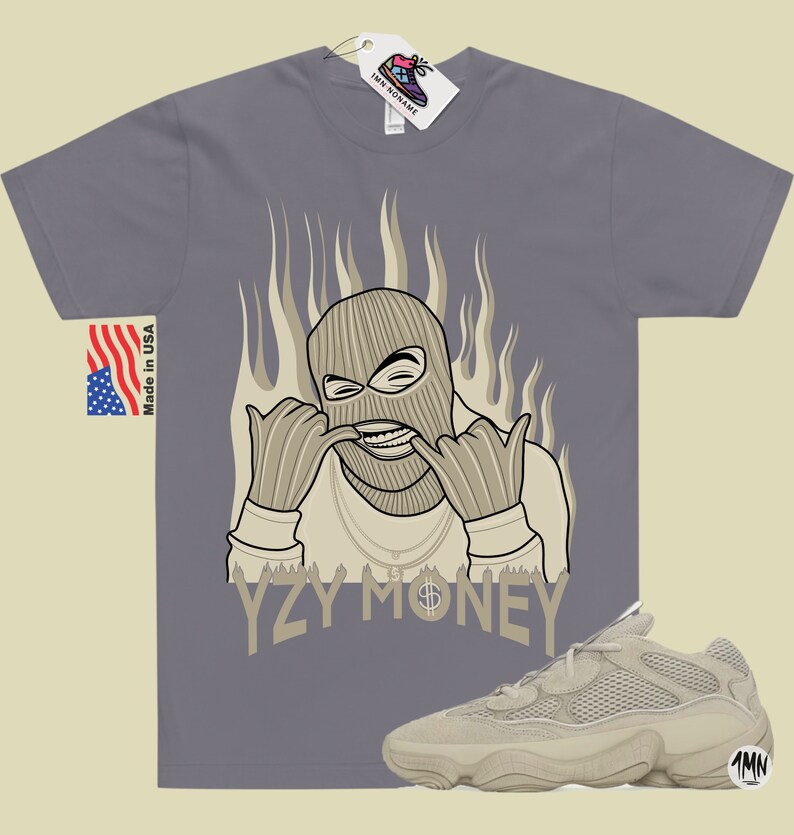 May include: A gray t-shirt with a cartoon illustration of a person wearing a ski mask and a gold chain. The text "YZY MONEY" is printed below the illustration. A pair of tan Yeezy 500 sneakers are shown in the bottom right corner of the image.