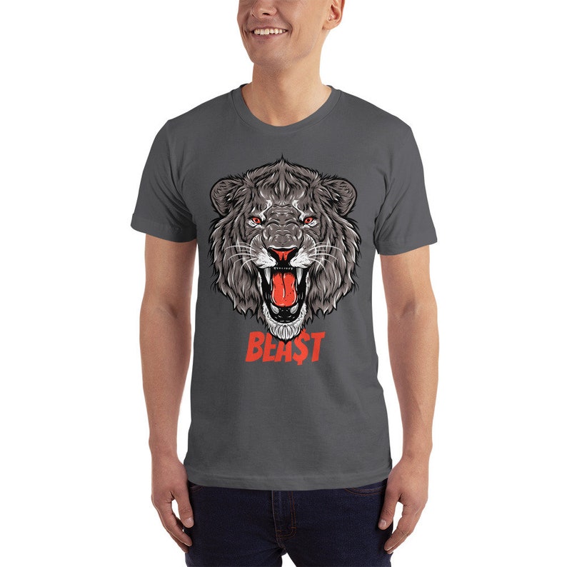 Puede incluir: Una camiseta gris oscuro con un gr&aacute;fico de una cabeza de le&oacute;n rugiente en blanco y negro con una lengua roja. El texto "BEAST" est&aacute; impreso en rojo debajo de la cabeza del le&oacute;n.