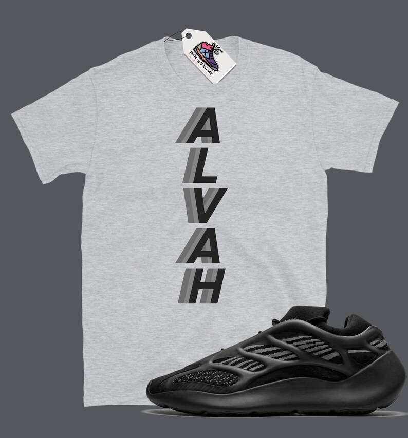 Puede incluir: Una camiseta gris con la palabra "ALVAH" impresa verticalmente en rayas negras y grises. Una zapatilla negra y gris se muestra debajo de la camiseta.