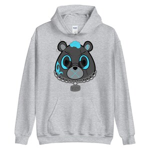 May include: A gray hoodie with a black and blue cartoon bear face graphic. The bear has a blue mohawk, blue eyes, a black nose, and a black mouth with an X over it. The bear is wearing a silver chain with a silver tag that says "VZY".