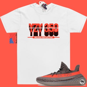 May include: White t-shirt with the text "YZY 350 BELUGA REFLECTIVE" in red and black. A pair of gray and orange Yeezy 350 sneakers are shown below the t-shirt.